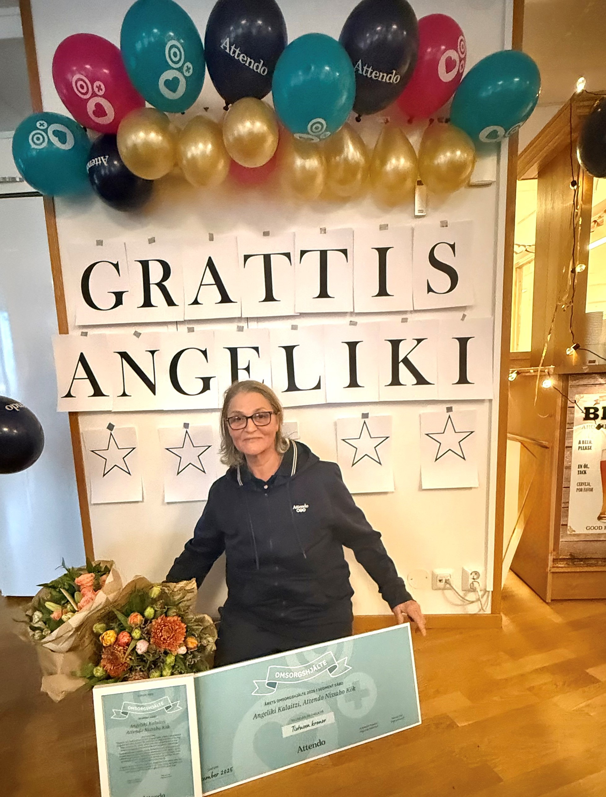 Angeliki sitter framför en stor grattisskylt, omringad av ballonger