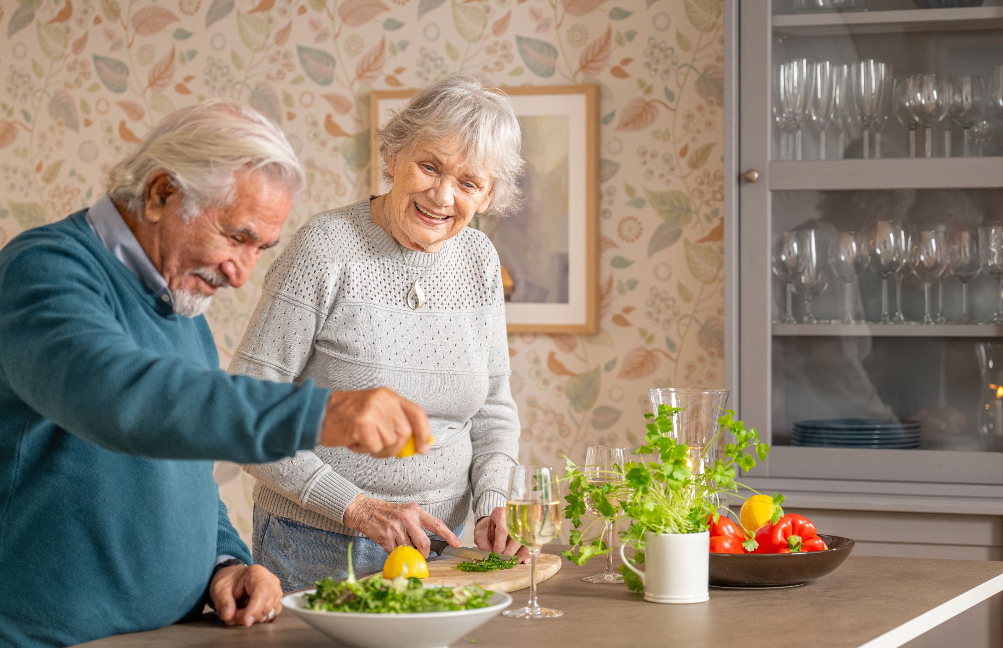 Man och kvinna kryddar sin mat som står på bänken, bredvid ett glas vin.