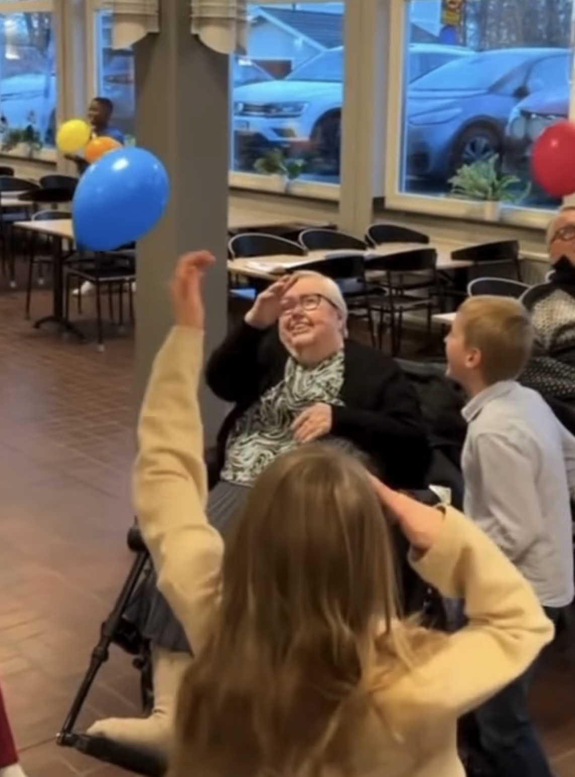 Äldre dam i rullstol leker med ballonger med eleverna och skrattar.