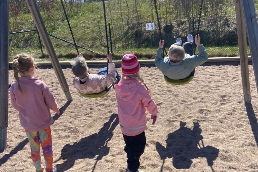 Två barn från förskolan ger fart åt två äldre damer på gungor.
