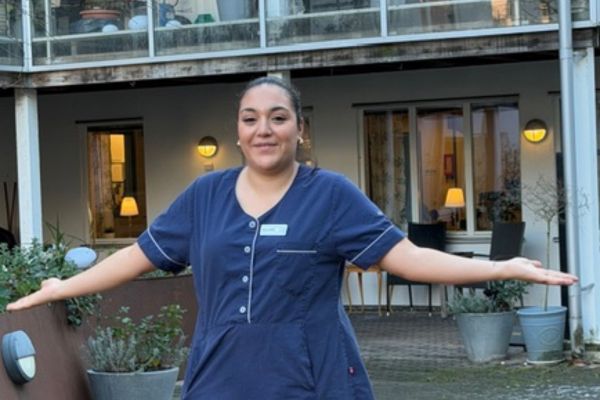 Undersköterskan Solange står stolt framför Attendo Västra Varvsgatan där hon jobbar, sträcker ut händerna