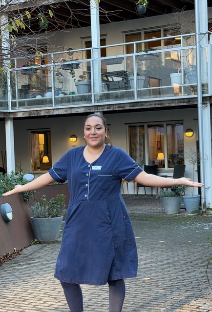 Undersköterskan Solange står stolt framför Attendo Västra Varvsgatan där hon jobbar, sträcker ut händerna