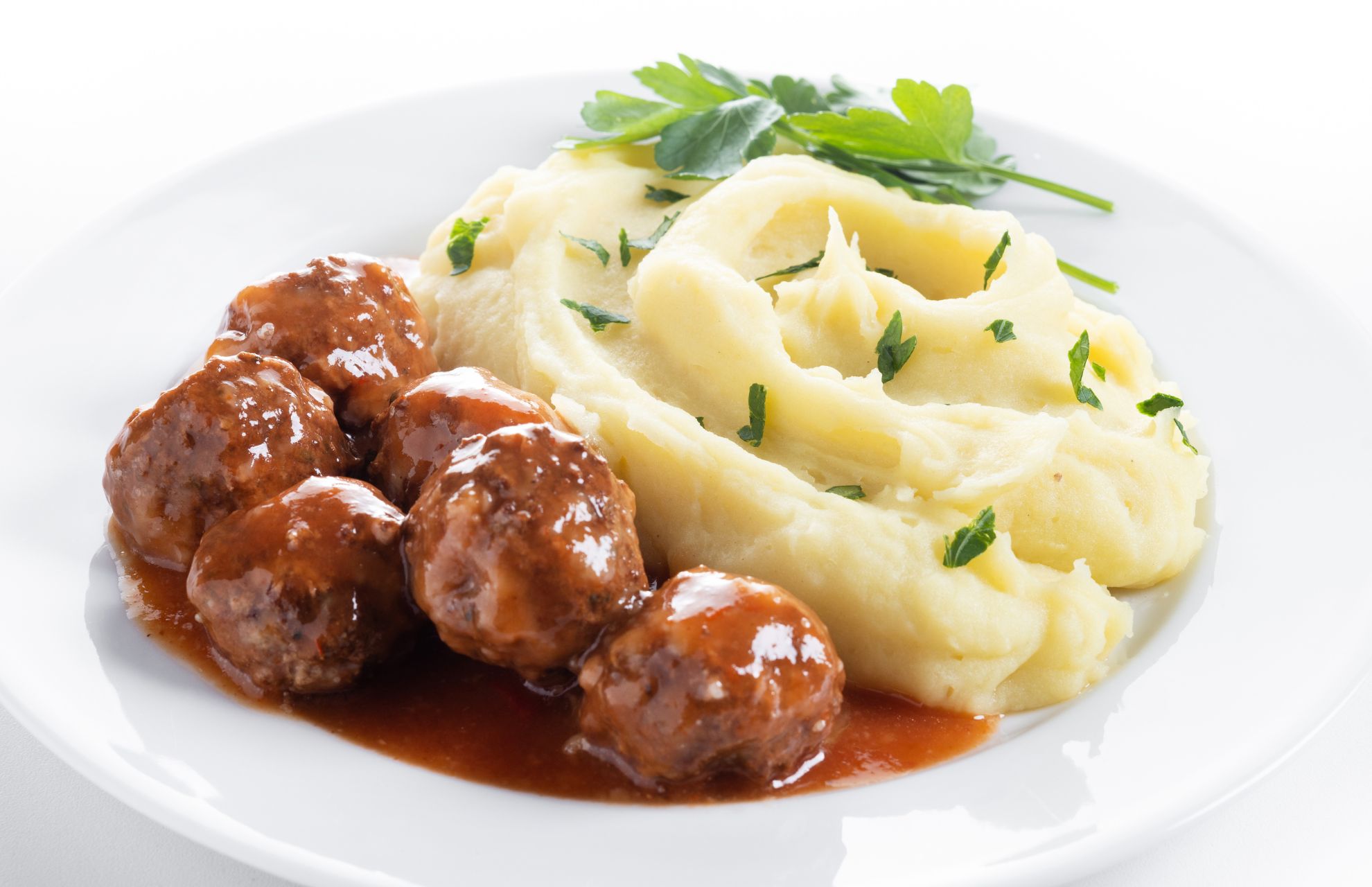 Köttbullar med potatis och brunsås och lite grönt, på vit tallrik