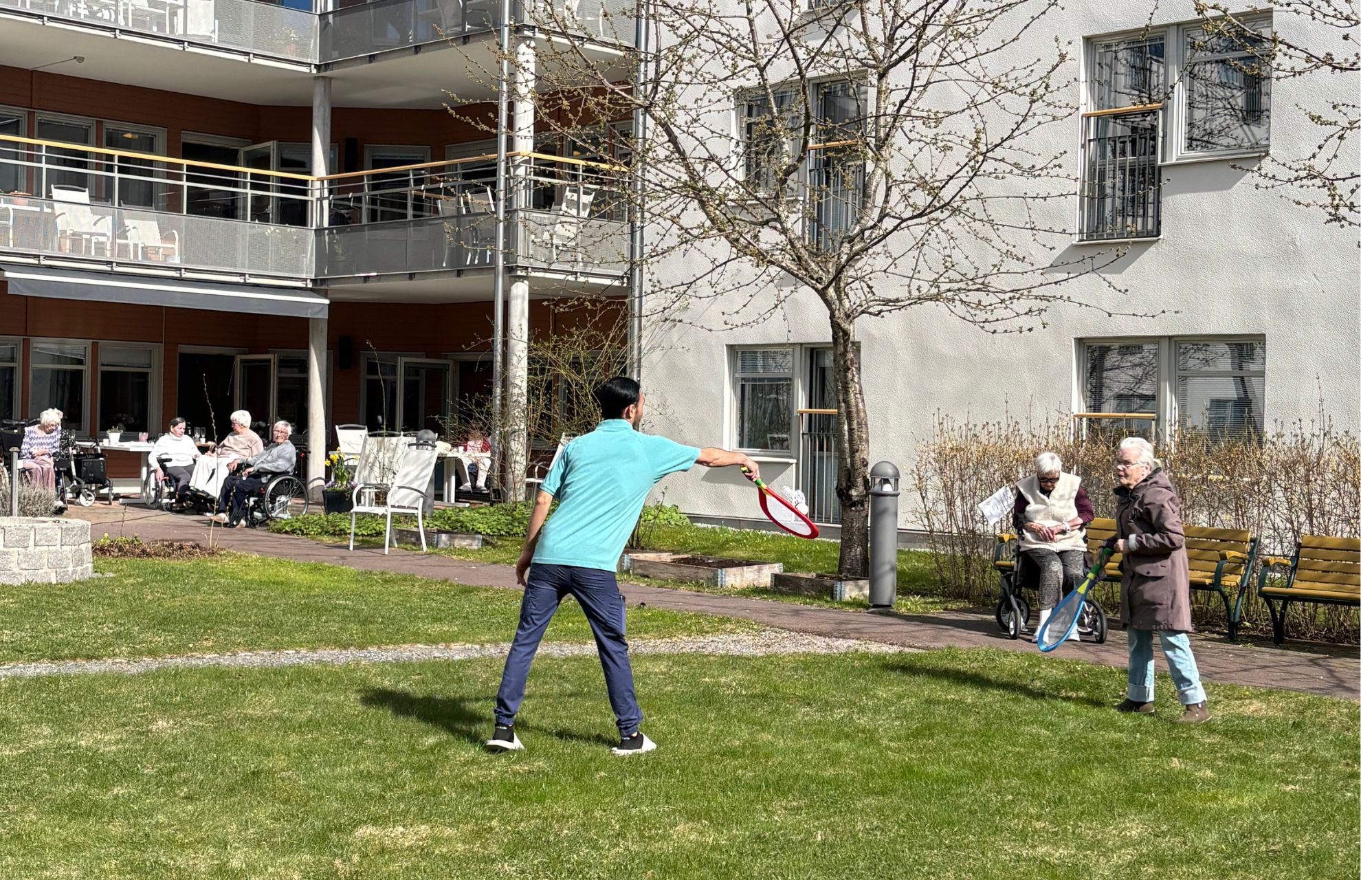 personal och boende spelar tennis tillsammans p&aring; solig innerg&aring;rd